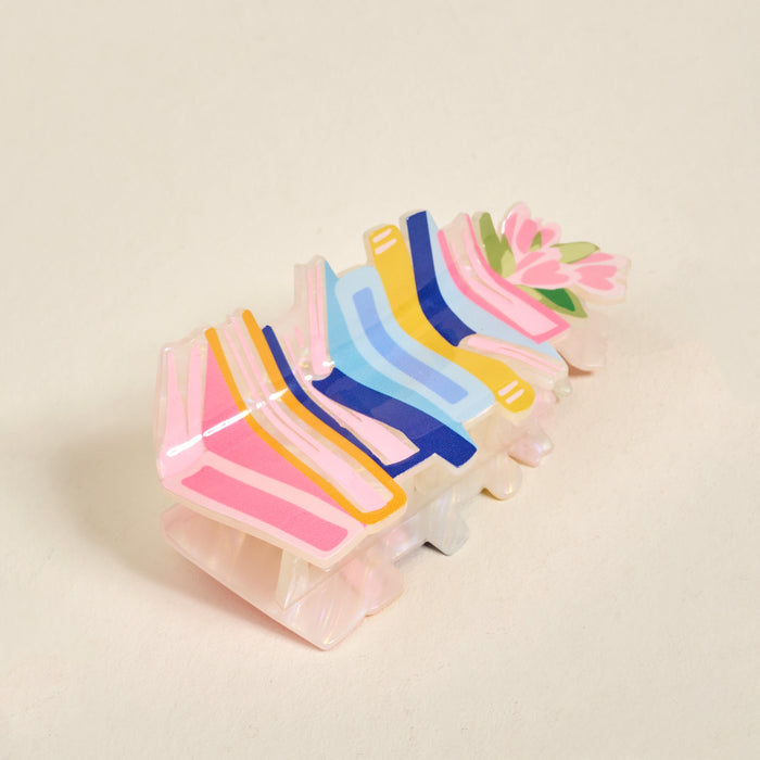 The Book Nook Shape Up Claw Clip by The Darling Effect showcases pastel pink, yellow, blue, and navy stripes in a floral design—perfect as a cute hair accessory to brighten up your favorite hairstyle.