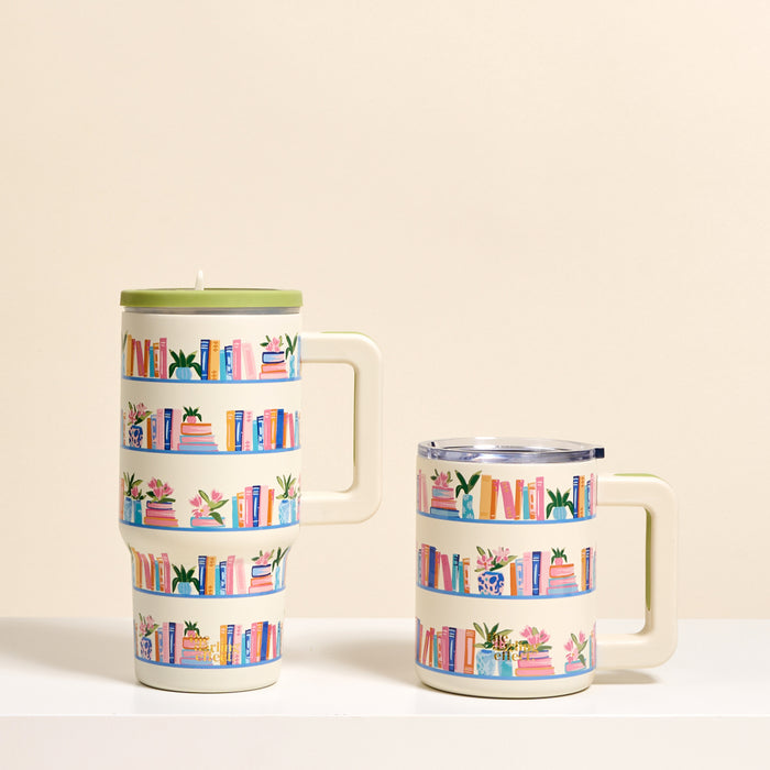 Two white "Book Shelfie" insulated mugs by The Darling Effect rest on a white surface, each featuring colorful bookshelf illustrations. The 14 oz mug has a green lid, while the shorter one has a clear lid and double-wall insulation.