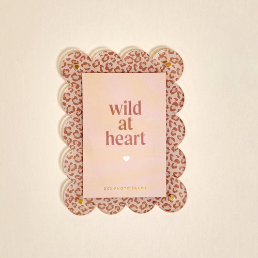 The Darling Effect's Born Wild Mini Acrylic Picture Frame Magnet features a scalloped pink leopard print and holds a card reading “wild at heart” with a white heart, making it a cute and decorative addition to your fridge.
