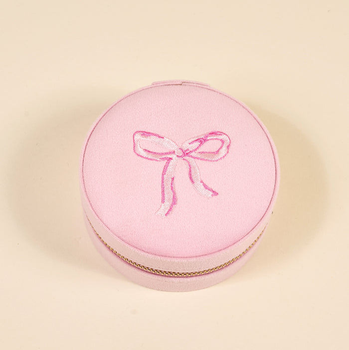 The Darling Effect Bow Pink Round Velvet Jewelry Case features a gold trim and an embroidered pink bow on the lid, shown here against a plain beige background.