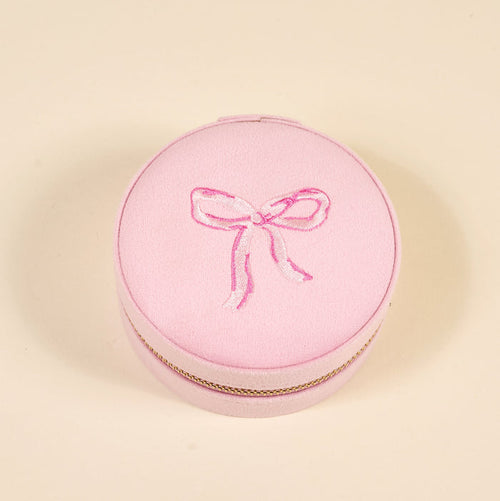 The Darling Effect Bow Pink Round Velvet Jewelry Case features a gold trim and an embroidered pink bow on the lid, shown here against a plain beige background.