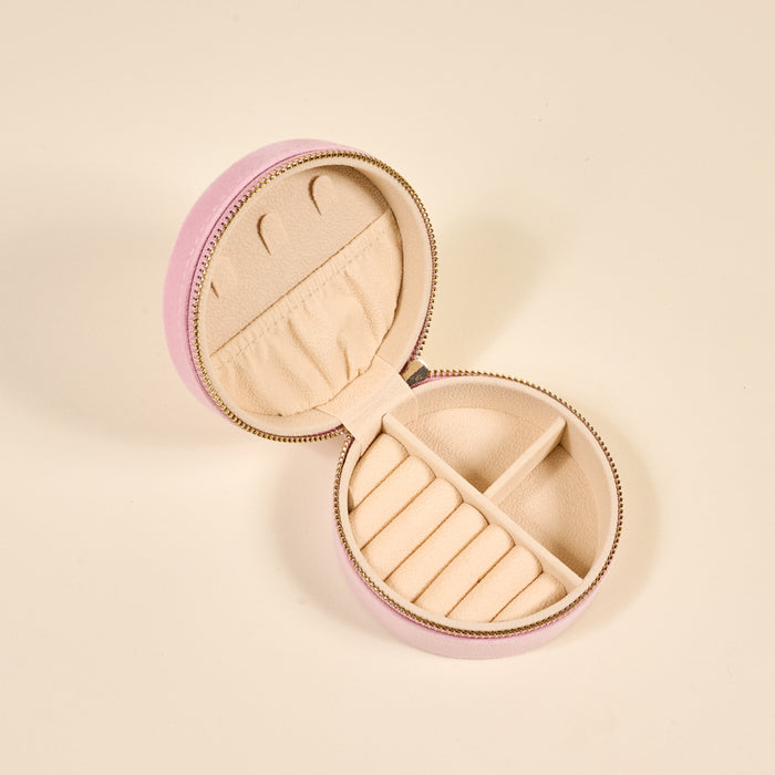 The Darling Effect’s Bow Pink Round Velvet Jewelry Case is open, showing a beige interior with ring slots and a zippered compartment for accessories.