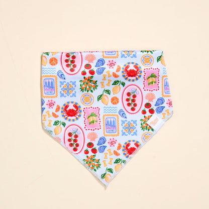 The Darling Effect Bow-Wow Pet Bandana-Ciao Bella is a vibrant cotton accessory with crabs, flowers, lemons, cherries, and shells on a light blue and white background—ideal for stylish pet fashion lovers.