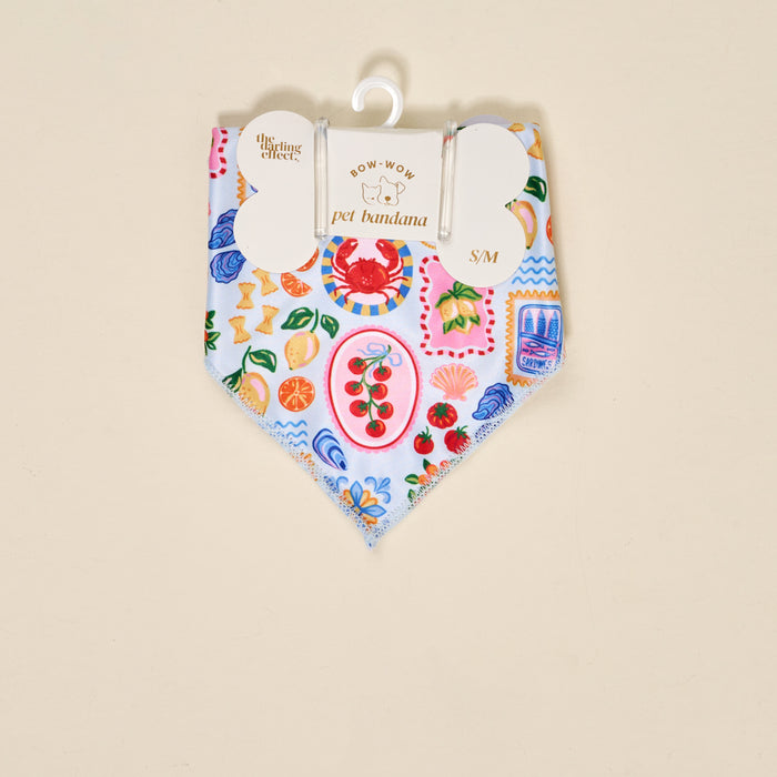 The Darling Effect Bow-Wow Pet Bandana-Ciao Bella (S/M) is a light blue cotton bandana for dogs with a vibrant Italian food-themed print, including crabs, tomatoes, pasta, lemons, and seafood. Displayed on a hanger with branded tag.