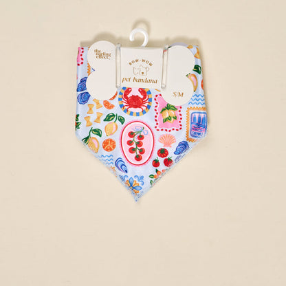 The Darling Effect Bow-Wow Pet Bandana-Ciao Bella (S/M) is a light blue cotton bandana for dogs with a vibrant Italian food-themed print, including crabs, tomatoes, pasta, lemons, and seafood. Displayed on a hanger with branded tag.