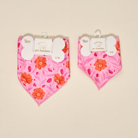 Two Bow-Wow Pet Bandana-Poppin' Petals Hot Pink by The Darling Effect, featuring red and orange floral prints, are displayed side by side on a cream background. The L/XL size is on the left, S/M on the right—both with hangers and tags.