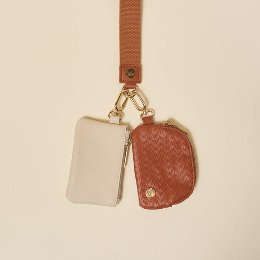 The Darling Effect’s Brown Dynamic Duo Pouch Luxe Wristlet features a tan strap with a cream zip pouch and a brown, rounded woven wristlet, both secured by gold clasps for a stylish hands-free accessory.