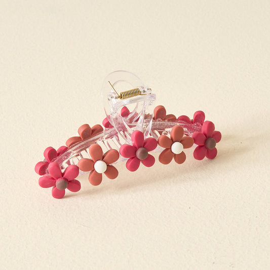 The Darling Effect Burgundy Game Day Daisy Claw Clip features clear plastic with burgundy and mauve flower designs, perfect for showing school colors or adding a fun pop to your Game Day outfit. Shown on a light cream-colored surface.