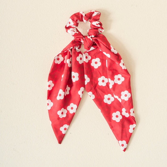 The Darling Effect’s Burgundy Game Day Hair Scarf with Scrunchie, showcasing white floral patterns and scarf-like tails, is perfect for displaying team spirit, shown here against a simple light background.