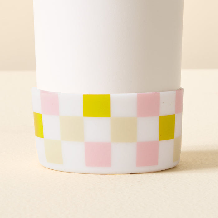A close-up of The Darling Effect's Check Green Tumbler Silicone Boot, shown on a white cylindrical tumbler. Its pastel pink, yellow, cream, and white checkerboard pattern wraps the base against a soft beige background.