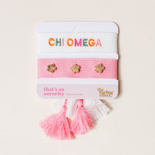 The Darling Effect's Chi Omega Woven Bracelet Set features two bracelets—one white with “CHI OMEGA” in colorful letters, one pink with gold flower studs—plus playful pink and white tassels, making a perfect sisterhood gift.
