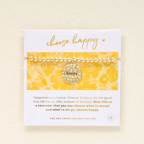 The Darling Effect's Choose Happy Beaded Charm Bracelet, featuring a gold beaded band and round charm with "HAPPY," is displayed on a yellow floral card—a thoughtful gift to inspire positivity and happiness each day.