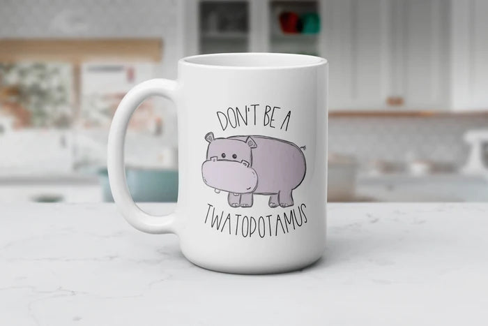 Chubby Cheeks & Petty Streaks white ceramic coffee mug featuring a cute purple hippo and the funny phrase “Don't Be a Twatopotamus,” available in 11 oz and 15 oz sizes.