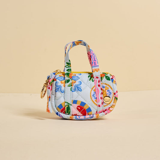 The Darling Effect Ciao Bella Itty Bitty Duffle Bag Charm is a small, quilted handbag with colorful floral and geometric patterns, gold zipper, two handles, and a quilted bag charm, shown on a plain beige background.