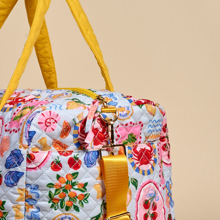 The Darling Effect's Ciao Bella On-the-Go Quilted Weekender Bag features bright yellow handles, an adjustable shoulder strap, and playful fruit and seashell patterns on a light background.