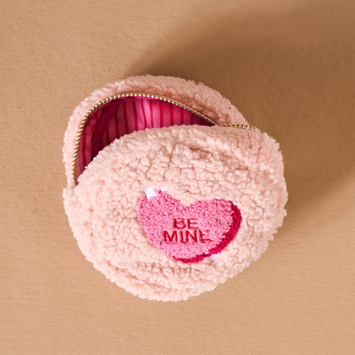 The Darling Effect’s Circle Be Mine Teddy Pouch is a round, fluffy pink sherpa pouch with a heart-shaped “BE MINE” patch and pink-striped lining from the Valentine’s Teddy Pouches collection.