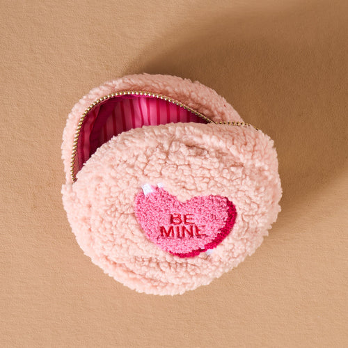 The Darling Effect’s Circle Be Mine Teddy Pouch is a round, fluffy pink sherpa pouch with a heart-shaped “BE MINE” patch and pink-striped lining from the Valentine’s Teddy Pouches collection.