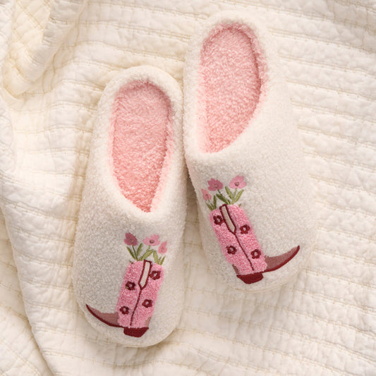 Cowgirl Boots Fuzzy Slippers by the-darling-effect feature pink interiors and embroidered pink cowboy boots with flowers, all resting on a cream-colored quilted blanket.