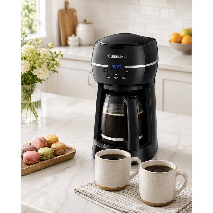Catalog scene of black Cuisinart DCC-1500FR coffee maker with filled carafe, two coffee cups, and macarons on a white kitchen counter.