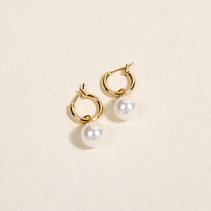 The Darling Effect’s Dainty Pearl Standout Earrings feature a high-shine golden hoop with a single round white pearl, shown against a light beige background.