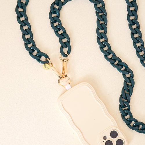 The Darling Effect's Dark Green Game Day Phone Chains feature a chunky chain with gold hardware, paired with a cream-colored wavy-edge case—perfect for elevating your game day style. Displayed on a light beige surface for added elegance.