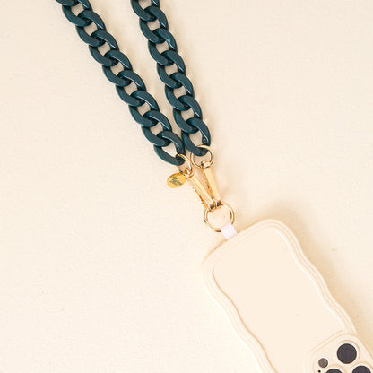 A close-up of The Darling Effect’s Dark Green Game Day Phone Chain with gold hardware, attached to a wavy-edged light phone case—stylishly displayed on a cream surface and perfect for your game day look.