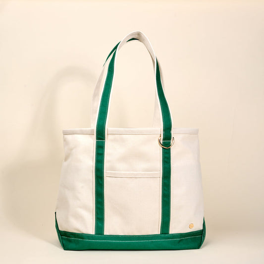 The Darling Effect's Dark Green The Signature Canvas Tote Bag features durable green handles, green trim, and a front pocket—perfect for daily use—displayed on a plain beige background.