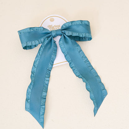 The Darling Effect's Dark Teal Ruffle Hair Bow features ruffled edges, attached to a white tag, and displayed on a light background.