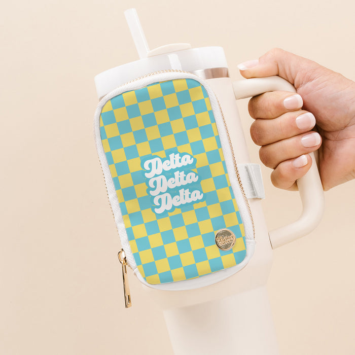 A hand holds The Darling Effect Delta Delta Delta Tumbler Fanny Pack: a white tumbler with handle and a water-resistant zippered pouch featuring a blue and yellow checkerboard design with “Delta Delta Delta” in white script.
