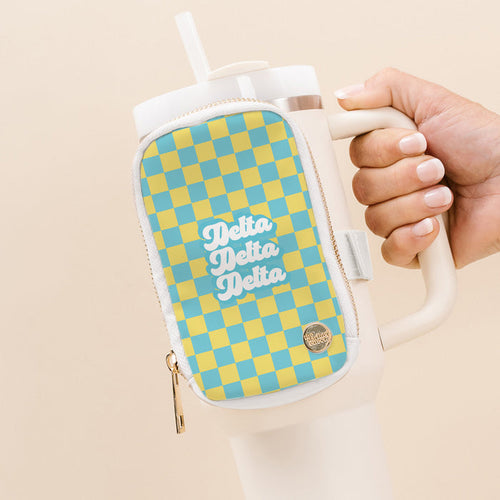 A hand holds The Darling Effect Delta Delta Delta Tumbler Fanny Pack: a white tumbler with handle and a water-resistant zippered pouch featuring a blue and yellow checkerboard design with “Delta Delta Delta” in white script.
