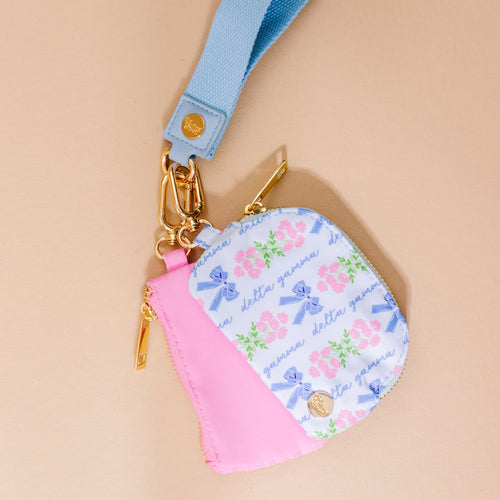The Darling Effect's Delta Gamma Dynamic Duo Pouch Wristlet is a small pastel pouch with a blue strap, gold hardware, pink, blue, and green floral patterns, Delta Gamma text on white, and a pink accent for hands-free style.