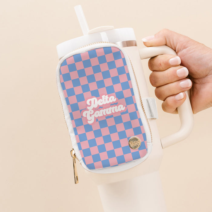A hand holds a large white tumbler with The Darling Effect's Delta Gamma Tumbler Fanny Pack, featuring water-resistant fabric, a pink and blue checkerboard pattern, and "Delta Gamma" in white script.
