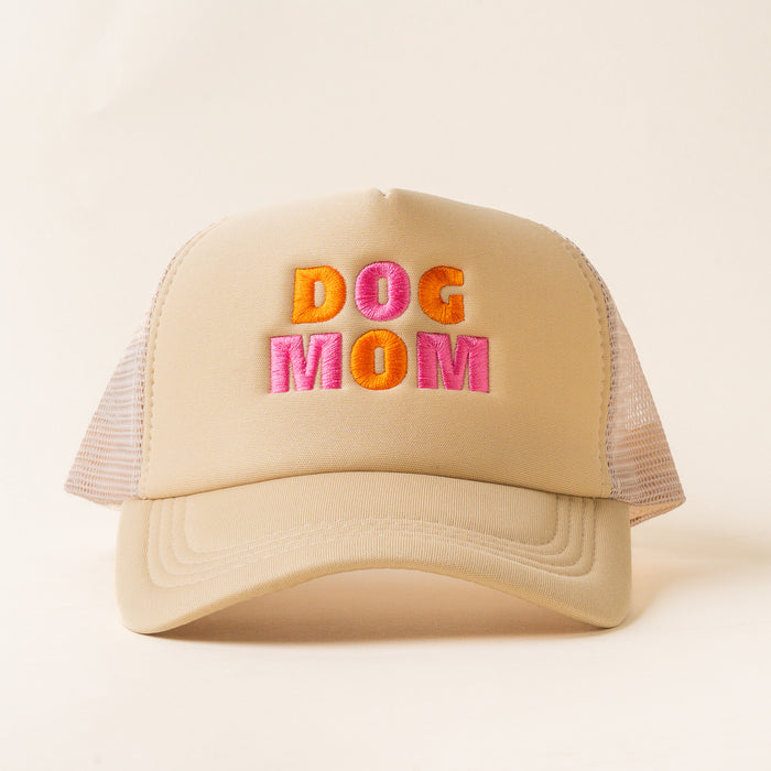 The Dog Mom Trucker Hat by the-darling-effect features bold orange and pink "DOG MOM" embroidery on beige with mesh sides. A trendy pick for dog lovers, it's shown against a plain, light background.