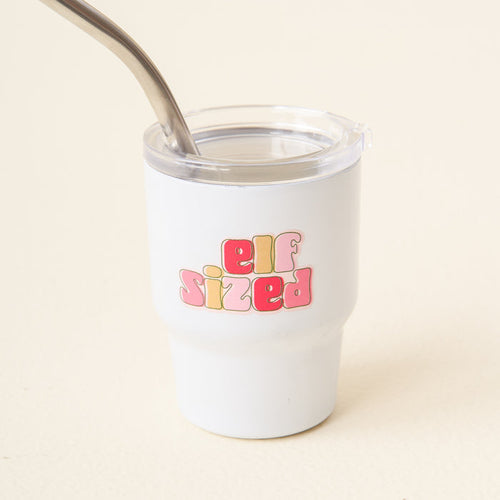 The-darling-effect's Elf Sized 2 oz Tiny Tumbler in white features "elf sized" in colorful bubble letters on the front and includes a clear lid and metal straw.