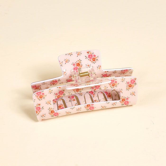 The Endless Daydream Cream Claw Clip by the-darling-effect features a pink print with red and green flowers, making it a stylish and practical hair accessory for any look. Photographed on a light beige surface.