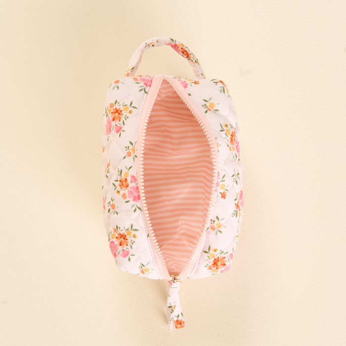 The Endless Daydream Cream Essentials Quilted Cosmetic Pouch by the-darling-effect features a white rectangular design with pink and orange floral patterns, a pink zipper, handle, and a striped interior—perfect for stylish travel makeup storage.