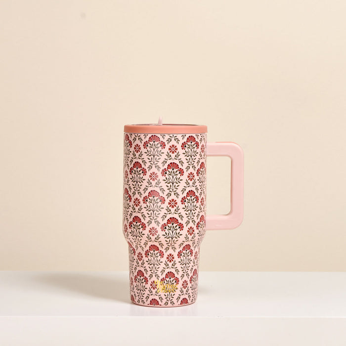 The Darling Effect Everbloom Dusty Rose 20 oz Lifestyle Flip Straw Tumbler, featuring a red and gray floral pattern and handle, sits on a white surface against a beige background. This insulated stainless steel mug keeps drinks perfectly hot or cold.