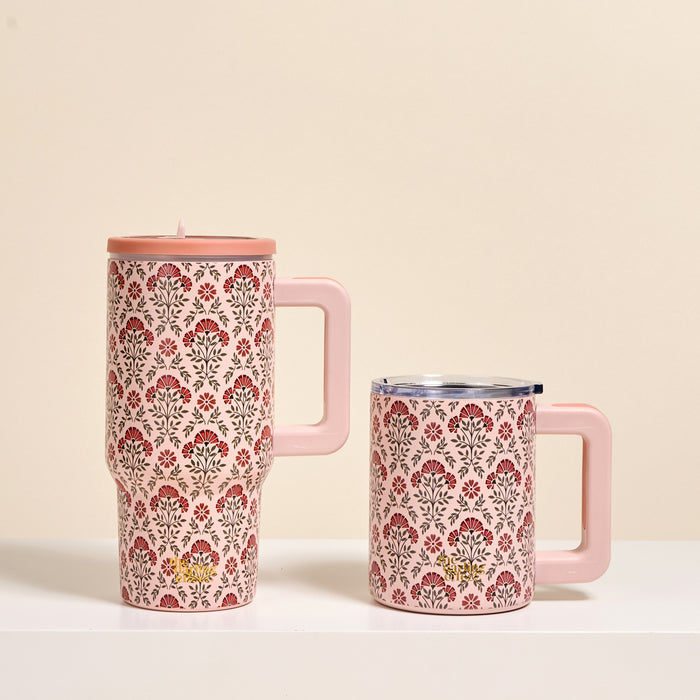 The Darling Effect’s Everbloom Dusty Rose 20 oz Lifestyle Flip Straw Tumbler with floral patterns and a lid stands next to a matching, smaller pink mug without a lid on a white surface.
