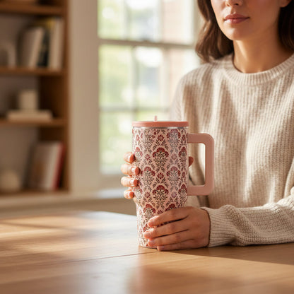 A woman in a cream sweater holds The Darling Effect Everbloom Dusty Rose 20 oz Lifestyle Flip Straw Tumbler, an insulated stainless steel tumbler with a floral pattern and pale pink handle and lid to keep drinks at the perfect temperature.