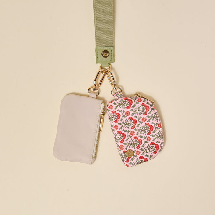 The Darling Effect Everbloom Dusty Rose Dynamic Duo Pouch Wristlet features a light green strap with a gold clasp, holding two pouches—one solid light gray zippered pouch and one pink and gray floral pouch—attached by gold keyring clips.
