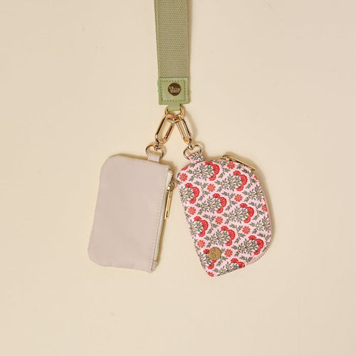 The Darling Effect Everbloom Dusty Rose Dynamic Duo Pouch Wristlet features a light green strap with a gold clasp, holding two pouches—one solid light gray zippered pouch and one pink and gray floral pouch—attached by gold keyring clips.
