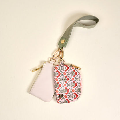 The Darling Effect’s Everbloom Dusty Rose Dynamic Duo Pouch Wristlet features two zippered pouches—one light pink, one white with red and grey florals—hanging from a green wristlet strap and secured with gold clasps for hands-free style.