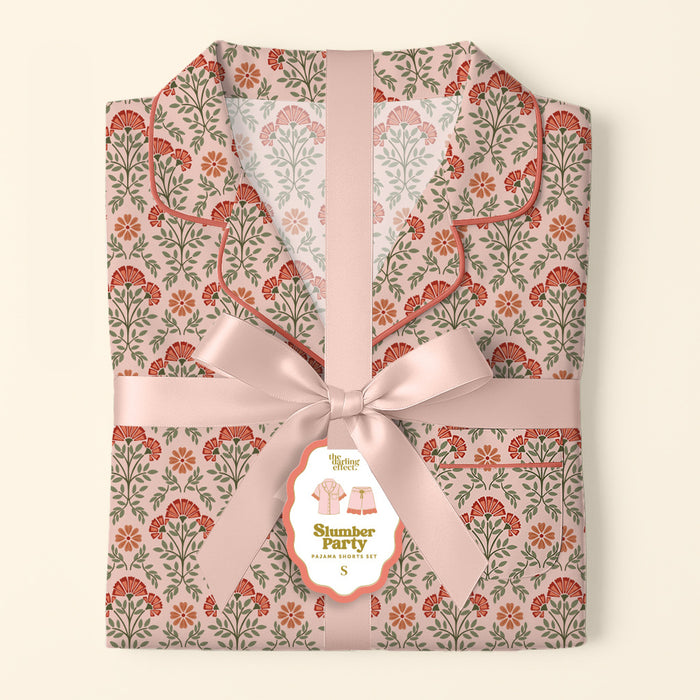 The Darling Effect’s Everbloom Dusty Rose Slumber Party Pajama Shorts Set features a pink and red floral pattern, tied with a wide pink satin ribbon and bow, plus a tag showcasing the relaxed fit and ultra-soft fabric.