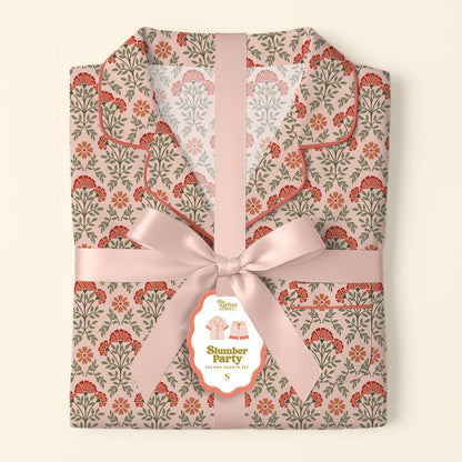 The Darling Effect’s Everbloom Dusty Rose Slumber Party Pajama Shorts Set features a pink and red floral pattern, tied with a wide pink satin ribbon and bow, plus a tag showcasing the relaxed fit and ultra-soft fabric.
