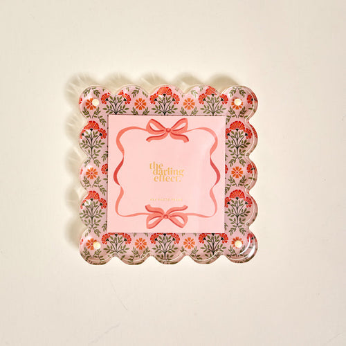 The Everbloom Dusty Rose Square Scalloped Acrylic Picture Frame by The Darling Effect features a decorative tray-like design with floral patterns, pink accents, and modern charm—perfect for displaying treasured memories.