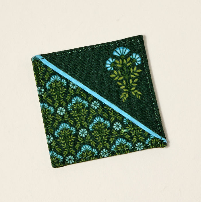 A square coaster with a diagonal blue stripe and a green leaf and blue flower pattern on dark green—great as a book lover gift or paired with The Darling Effect’s Everbloom Forest Green Corner Keeper Fabric Bookmark.