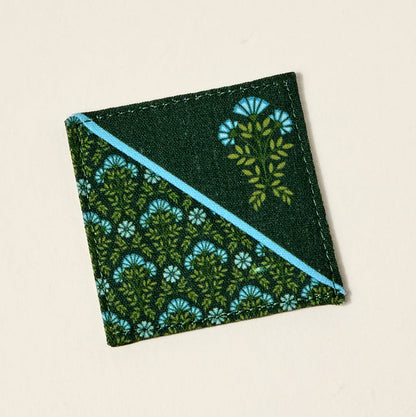 A square coaster with a diagonal blue stripe and a green leaf and blue flower pattern on dark green—great as a book lover gift or paired with The Darling Effect’s Everbloom Forest Green Corner Keeper Fabric Bookmark.