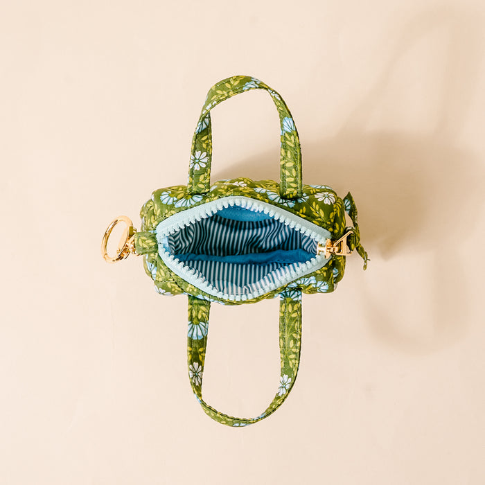 The Darling Effect’s Everbloom Forest Green Itty Bitty Duffle Bag Charm is shown open on a light beige background, featuring a blue striped interior—perfect as a stylish accessory or paired with other bag charms for extra flair.