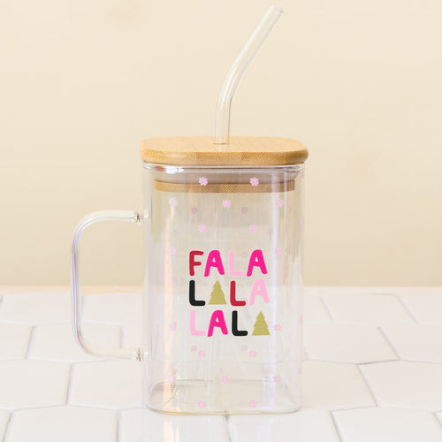 The Darling Effect Fa La La Square Glass Cup is a clear iridescent glass mug with a handle, bamboo lid, and glass straw. It features “FALALALALA” in colorful letters, Christmas trees, pink snowflakes, and is shown on a white tiled surface.