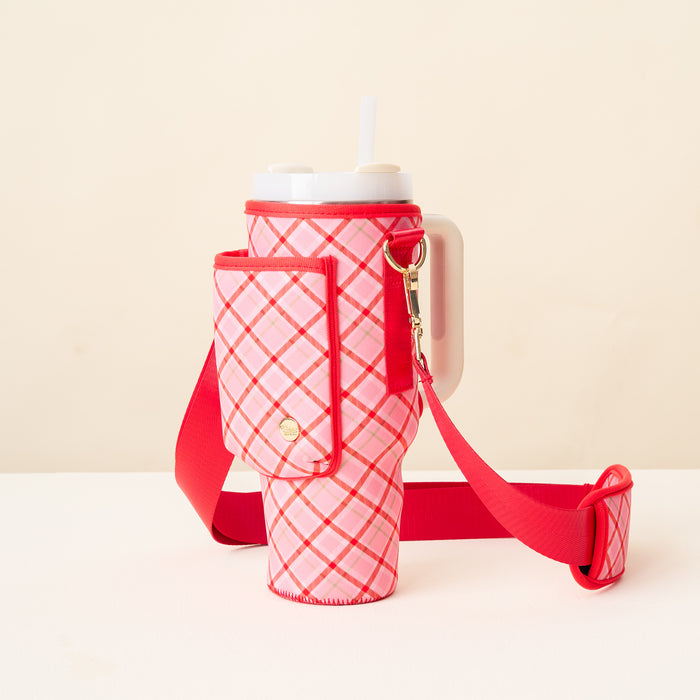 The Darling Effect's Festive Plaid Tumbler Sling, featuring a pink and red plaid design, gold clasp, matching adjustable strap, and attached pouch, holds a large tumbler with white lid and straw against a neutral background.